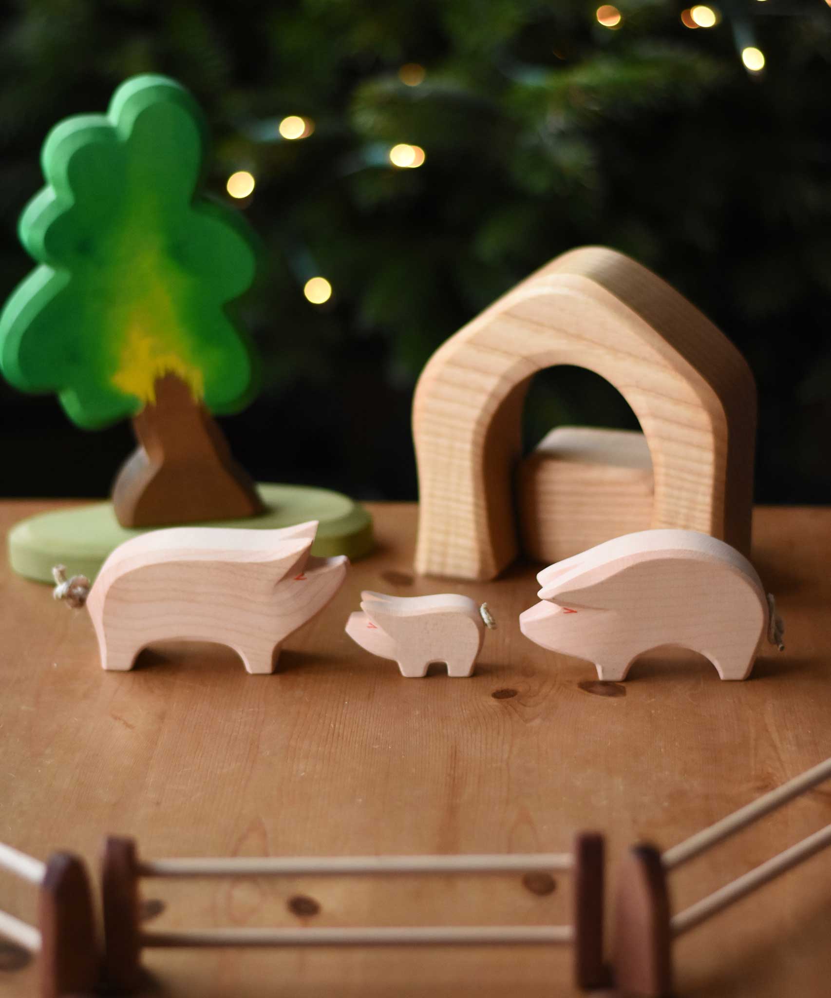Ostheimer wooden toy pink pig and piglet figures set up in a small world play scene with the Ostheimer oak tree, fences and pieces from the 4 piece house set. These wooden figures are part of a wide range of expertly hand crafted wooden toys here at Babipur. 