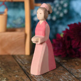 An Ostheimer hand made wooden Lady-In-Waiting toy figure placed on a wooden surface in a small world play scene. Other wooden toys including an Ostheimer water well can be seen in the background. These wooden figures are part of a wide range of expertly hand crafted wooden toys here at Babipur. 