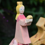 An Ostheimer pink princess for frog prince wooden toy figure held up in an adult's hand to show scale. This wooden figure is part of a large range of expertly hand crafted, Waldorf inspired, wooden toys here at Babipur. 
