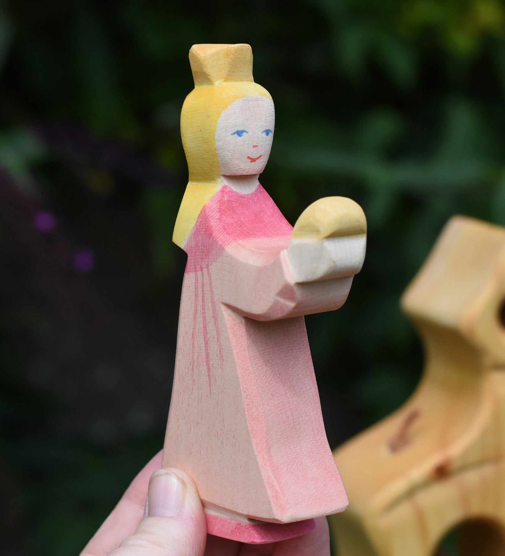 An Ostheimer pink princess for frog prince wooden toy figure held up in an adult's hand to show scale. This wooden figure is part of a large range of expertly hand crafted, Waldorf inspired, wooden toys here at Babipur. 