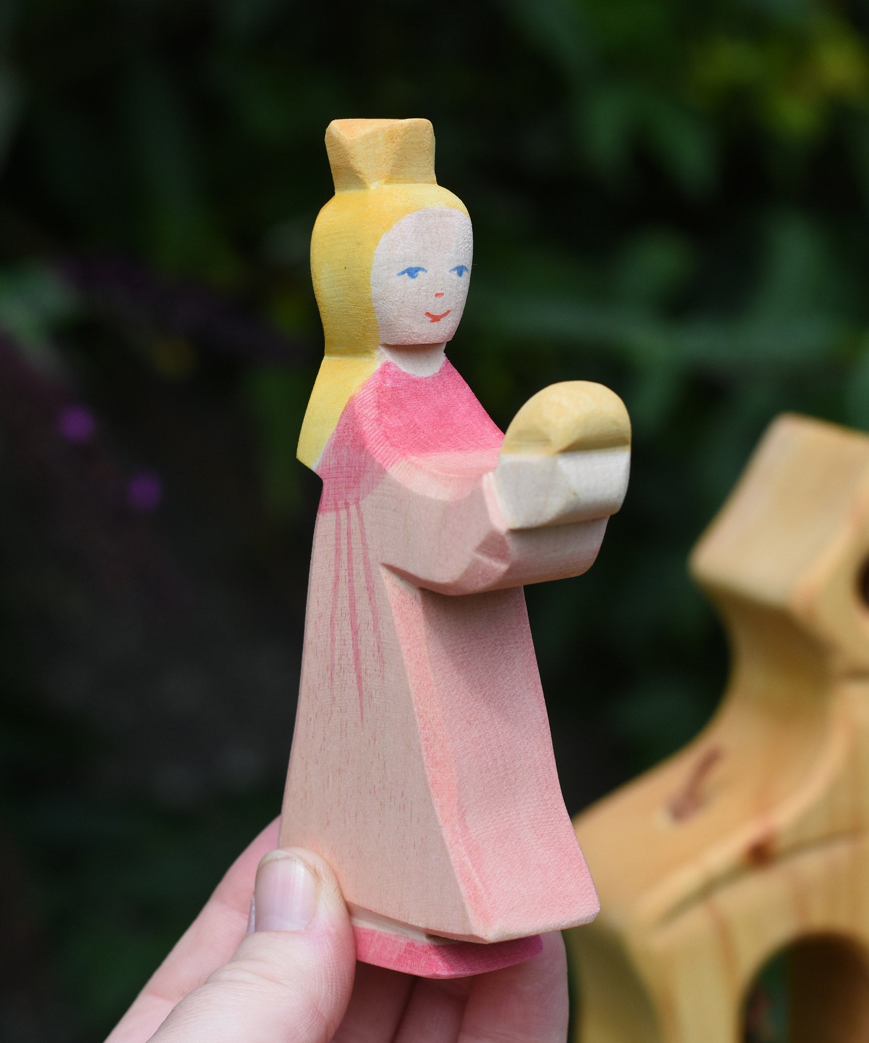 An Ostheimer pink princess for frog prince wooden toy figure held up in an adult's hand to show scale. This wooden figure is part of a large range of expertly hand crafted, Waldorf inspired, wooden toys here at Babipur. 
