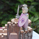 An Ostheimer pink standing knight with decorated shield and grey sword placed on a piece of the Magic Wood castle. This wooden figure is part of a large range of expertly hand crafted wooden toys here at Babipur. 