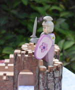 An Ostheimer pink standing knight with decorated shield and grey sword placed on a piece of the Magic Wood castle. This wooden figure is part of a large range of expertly hand crafted wooden toys here at Babipur. 
