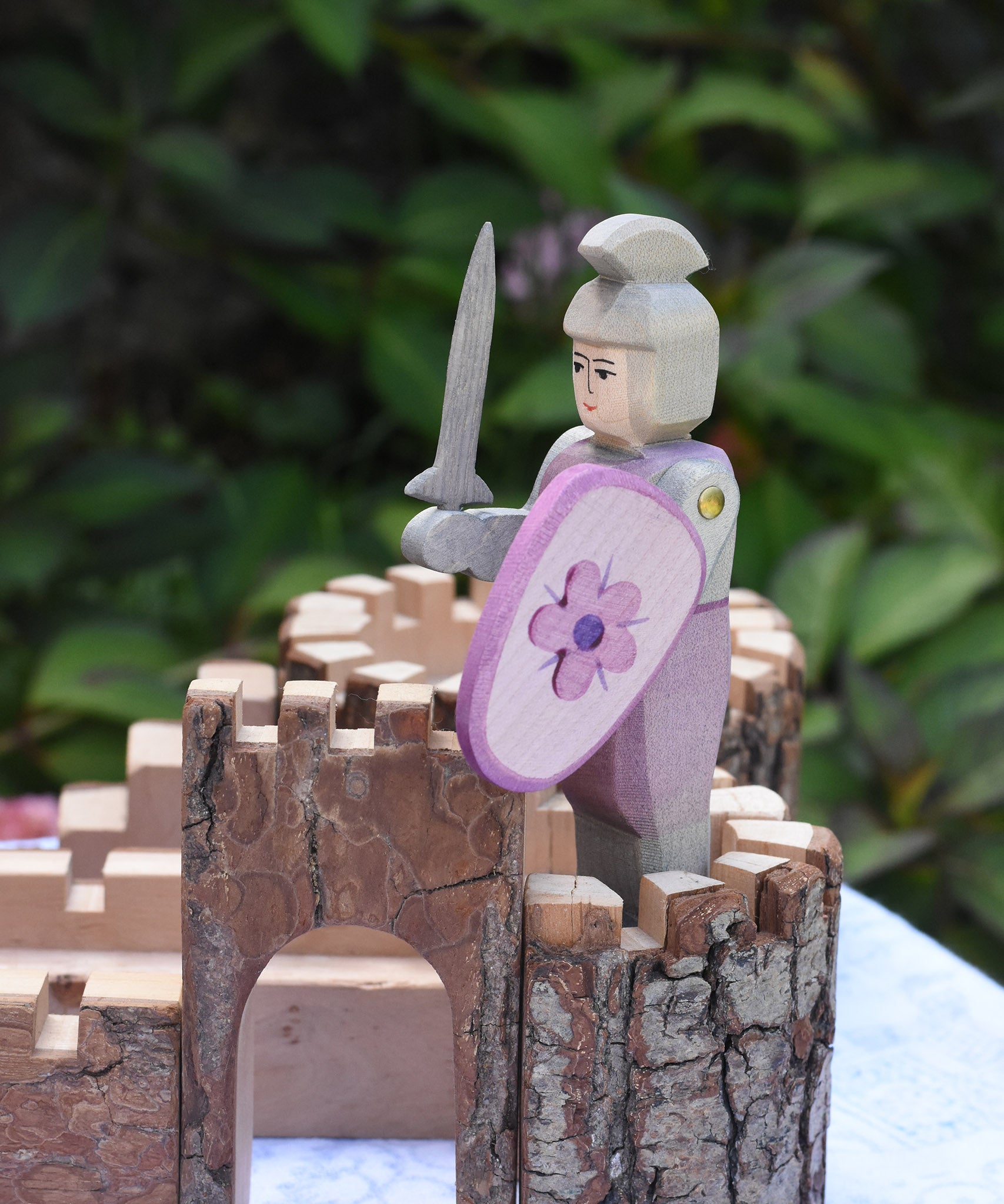 An Ostheimer pink standing knight with decorated shield and grey sword placed on a piece of the Magic Wood castle. This wooden figure is part of a large range of expertly hand crafted wooden toys here at Babipur. 