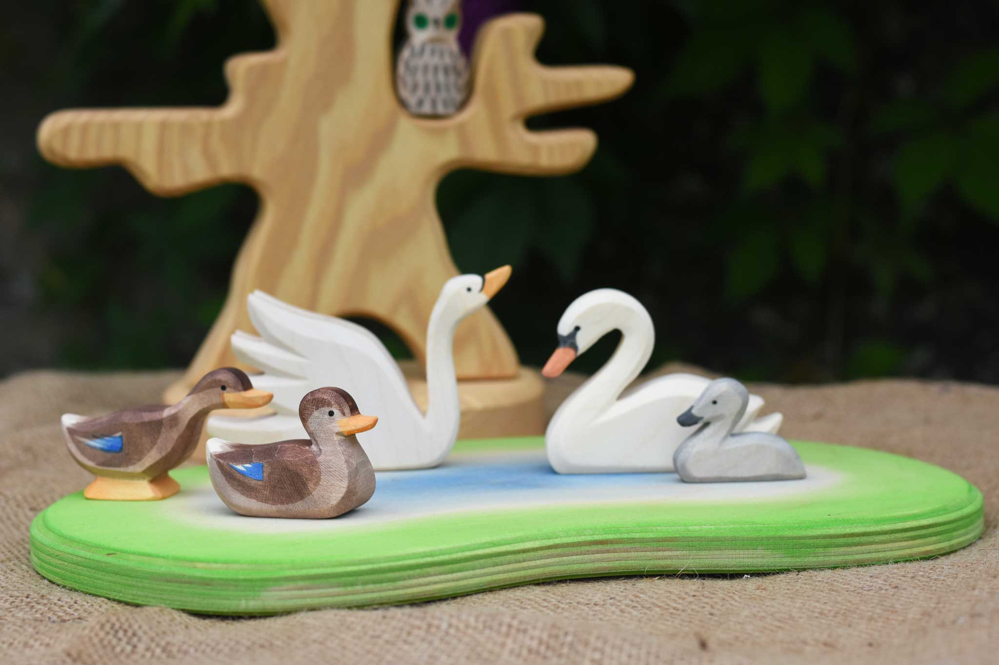 An Ostheimer wooden pond placed in the centre of a small world play scene with Ostheimer duck and swan figures. An Ostheimer bird tree can be seen in the background. 