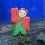 An Ostheimer hand made and hand painted wooden poppy Flower Child figure toy placed on a stone wall outdoors. These flower child wooden figures are part of a wide range of expertly hand crafted wooden toys here at Babipur. 