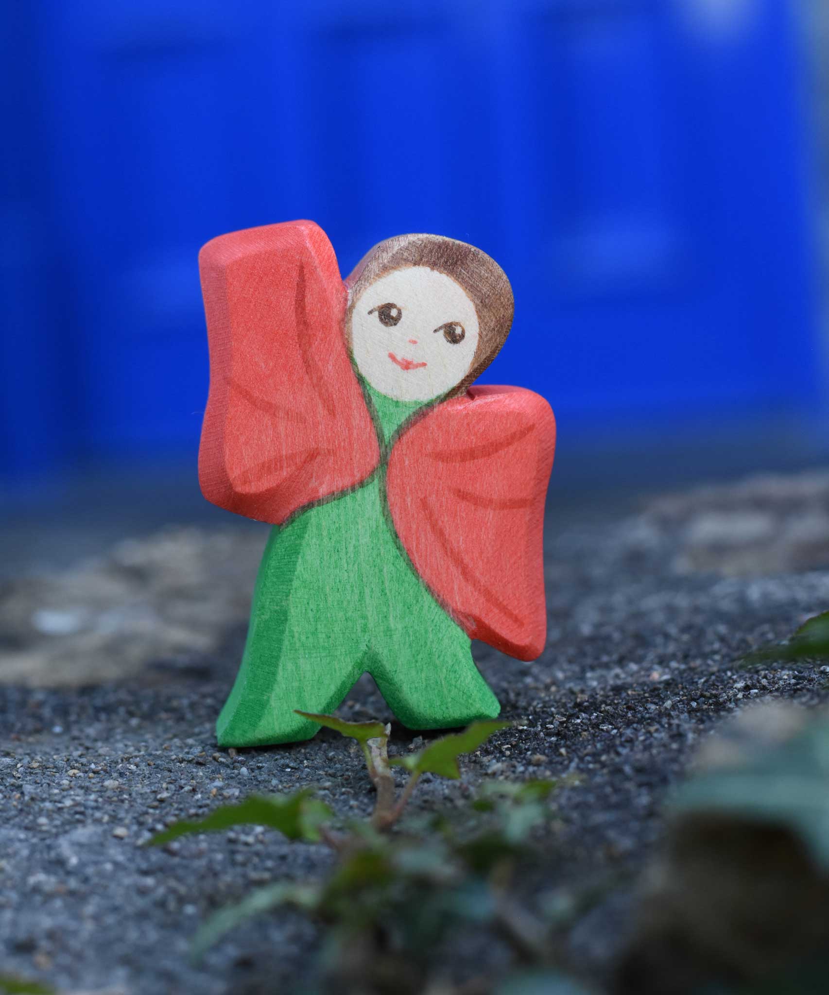 An Ostheimer hand made and hand painted wooden poppy Flower Child figure toy placed on a stone wall outdoors. These flower child wooden figures are part of a wide range of expertly hand crafted wooden toys here at Babipur. 