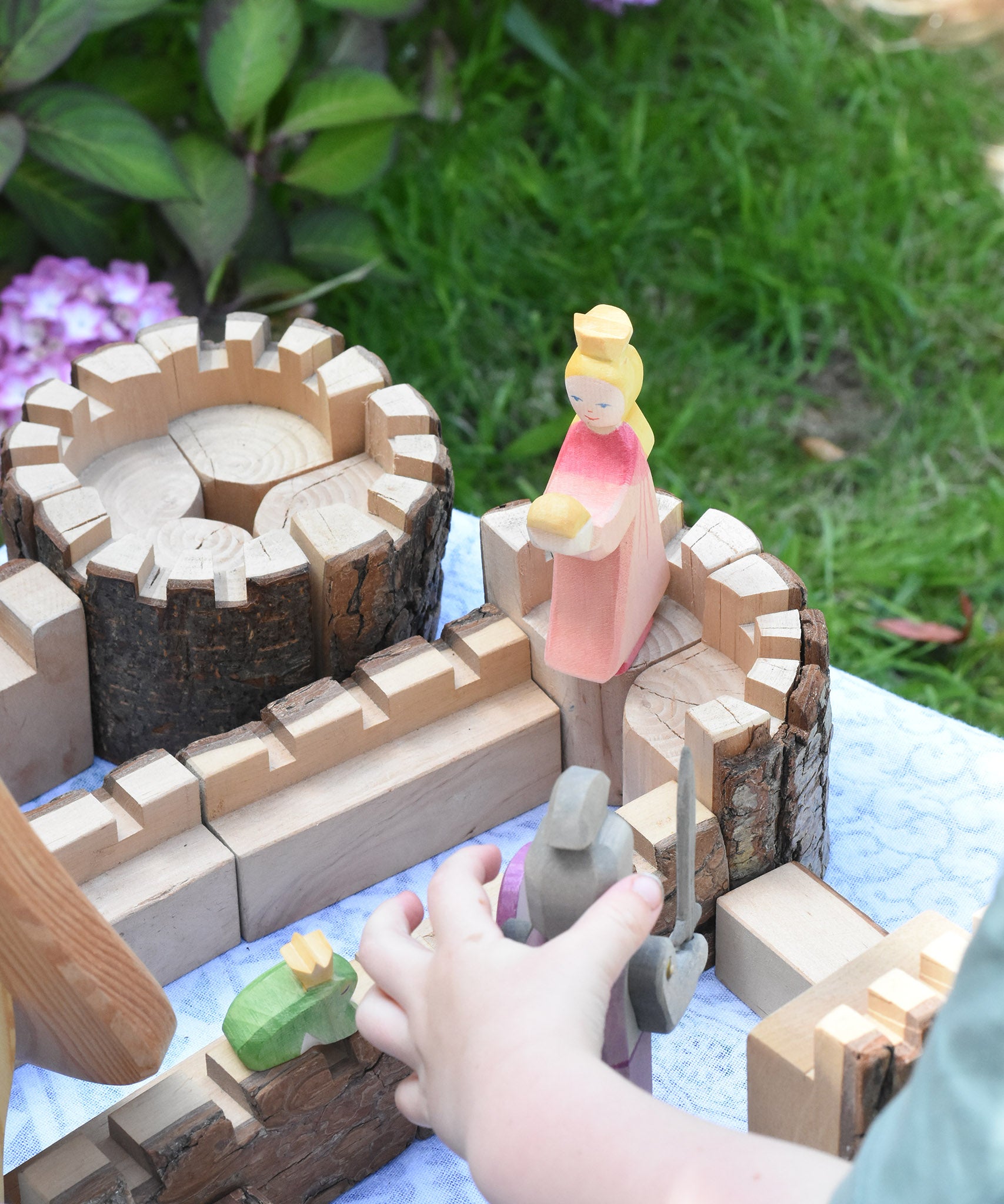 An Ostheimer pink princess for frog prince wooden toy figure placed on a turret of the Magic Wood castle. This wooden figure is part of a large range of expertly hand crafted, Waldorf inspired, wooden toys here at Babipur. 