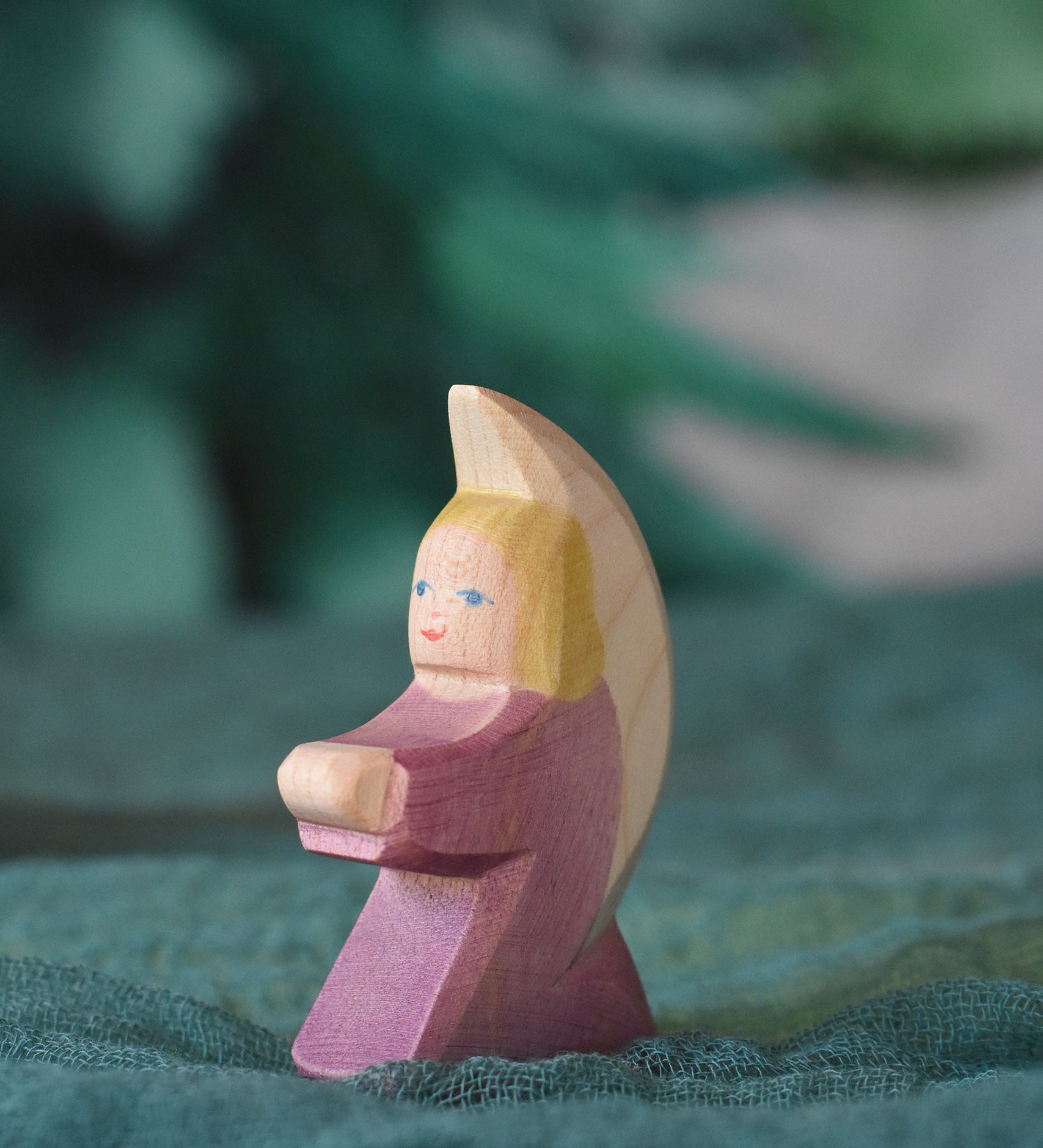 A purple coloured little Ostheimer angel placed on a green decoration scarf. This wooden figure is part of a large range of expertly hand crafted, Waldorf inspired, wooden toys here at Babipur.