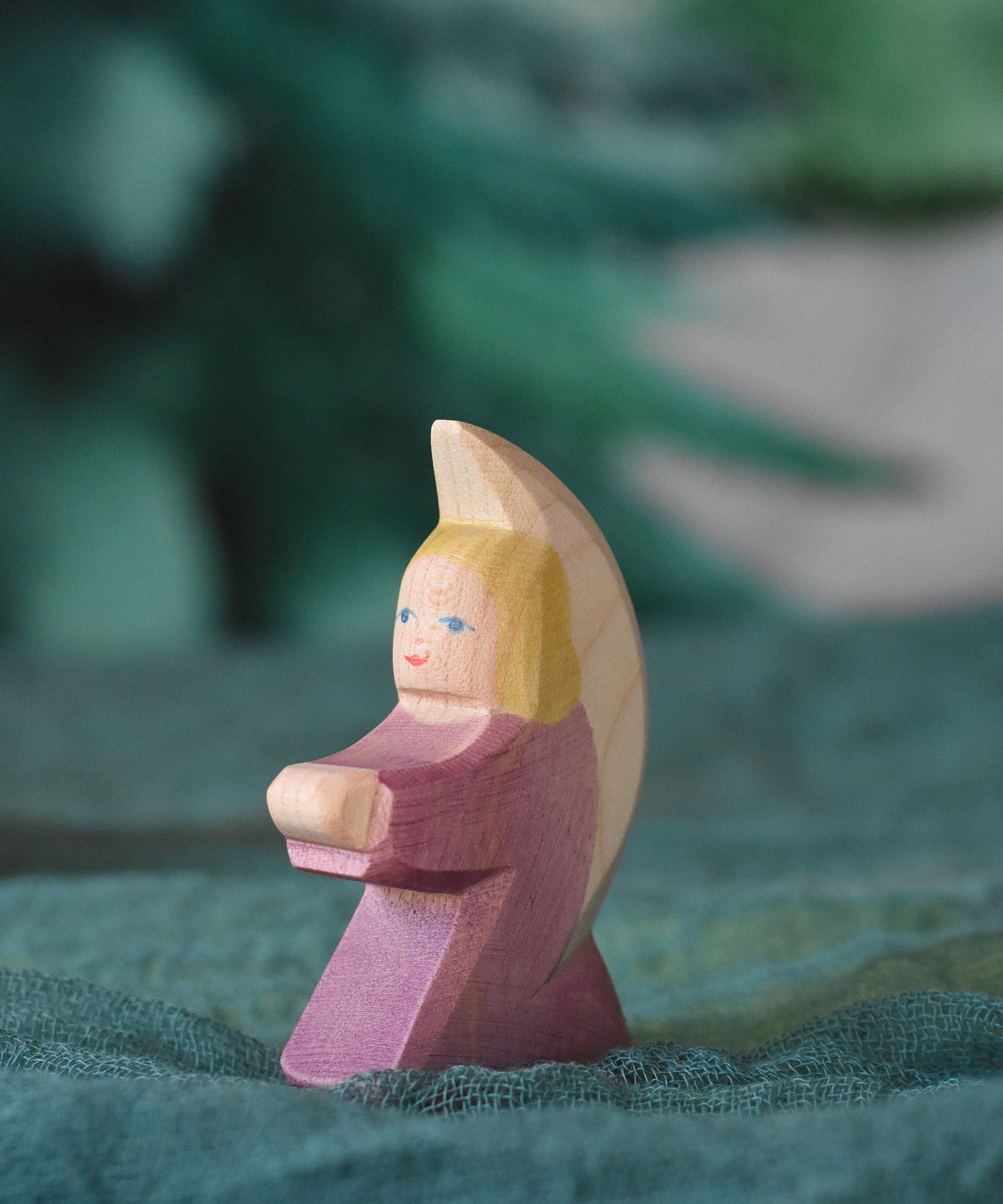 A purple coloured little Ostheimer angel placed on a green decoration scarf. This wooden figure is part of a large range of expertly hand crafted, Waldorf inspired, wooden toys here at Babipur.