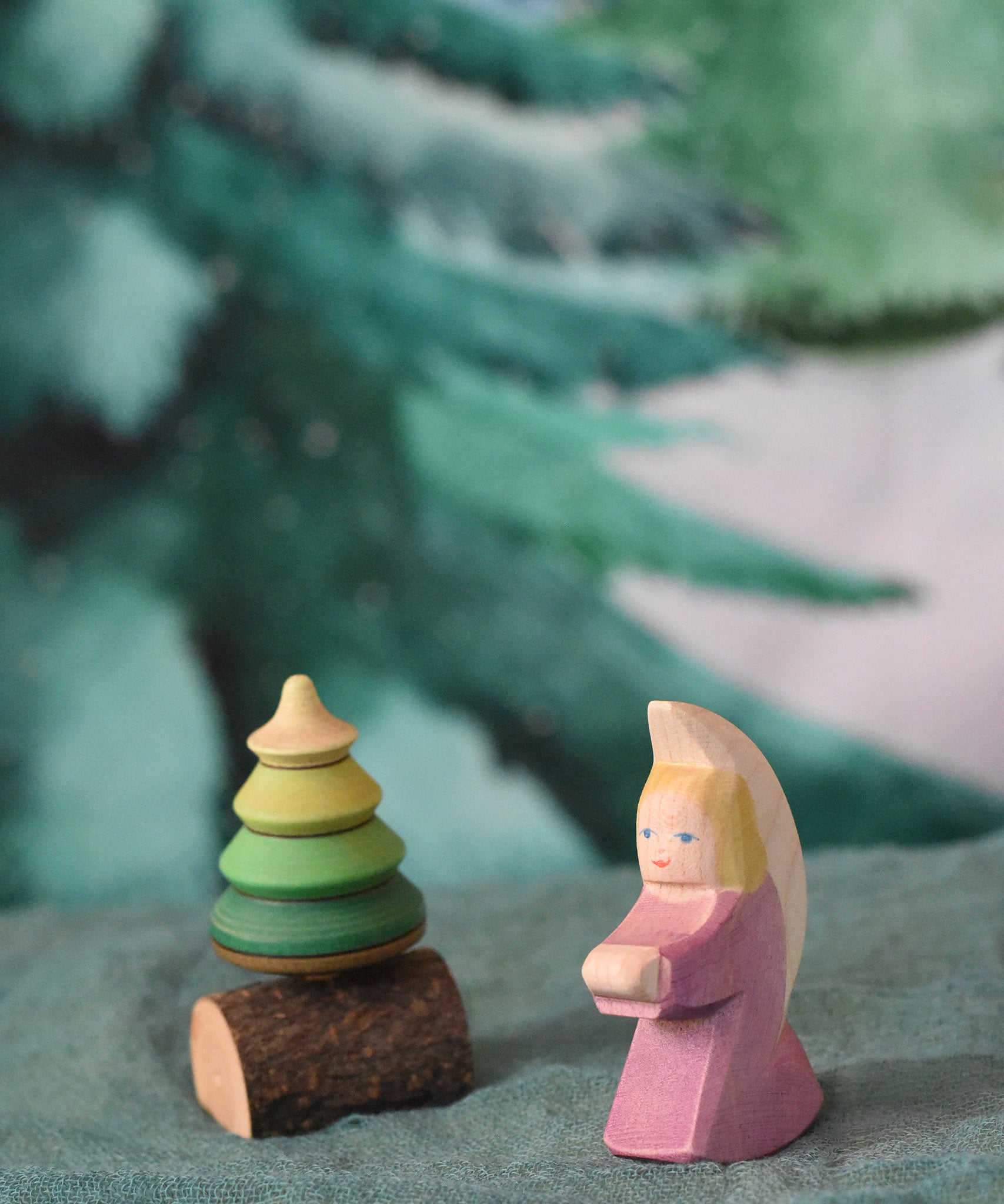 A purple coloured Ostheimer little angel placed on a green coloured decoration scarf next to a Mader spinner. This wooden figure is part of a large range of expertly hand crafted, Waldorf inspired, wooden toys here at Babipur.