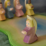 A purple Ostheimer angel placed on an Ostheimer pond scene piece. Other little angels can be seen in the background. This wooden figure is part of a large range of expertly hand crafted, Waldorf inspired, wooden toys here at Babipur.