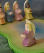 A purple Ostheimer angel placed on an Ostheimer pond scene piece. Other little angels can be seen in the background. This wooden figure is part of a large range of expertly hand crafted, Waldorf inspired, wooden toys here at Babipur.