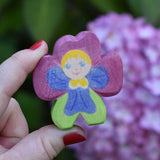 An Ostheimer hand made and hand painted wooden pansy Flower Child figure toy held in an adult's hand to show scale. These flower child wooden figures are part of a wide range of expertly hand crafted wooden toys here at Babipur. 
