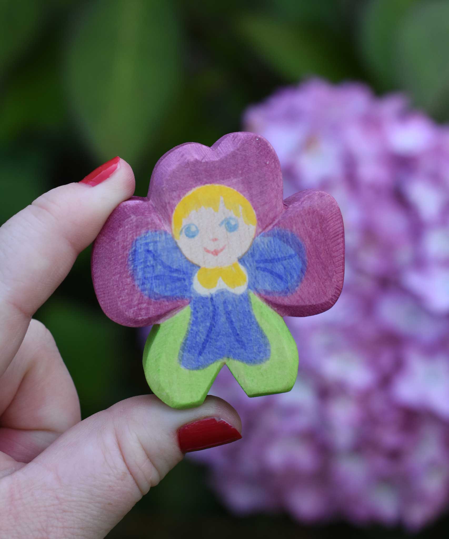 An Ostheimer hand made and hand painted wooden pansy Flower Child figure toy held in an adult's hand to show scale. These flower child wooden figures are part of a wide range of expertly hand crafted wooden toys here at Babipur. 
