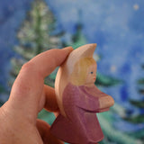 A purple coloured Ostheimer little angel held in an adult's hand to show scale. This wooden figure is part of a large range of expertly hand crafted, Waldorf inspired, wooden toys here at Babipur. 