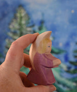 A purple coloured Ostheimer little angel held in an adult's hand to show scale. This wooden figure is part of a large range of expertly hand crafted, Waldorf inspired, wooden toys here at Babipur. 