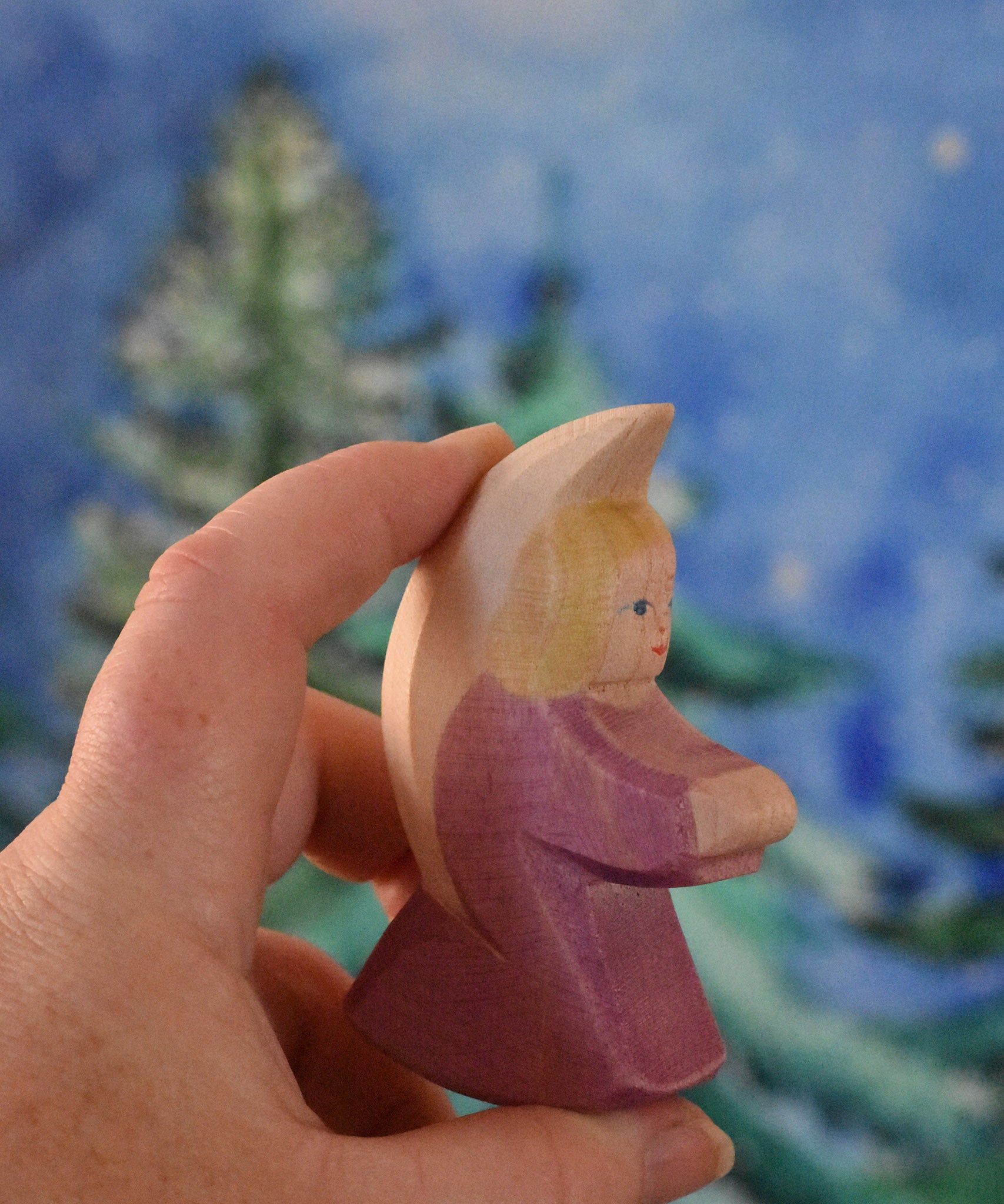 A purple coloured Ostheimer little angel held in an adult's hand to show scale. This wooden figure is part of a large range of expertly hand crafted, Waldorf inspired, wooden toys here at Babipur. 