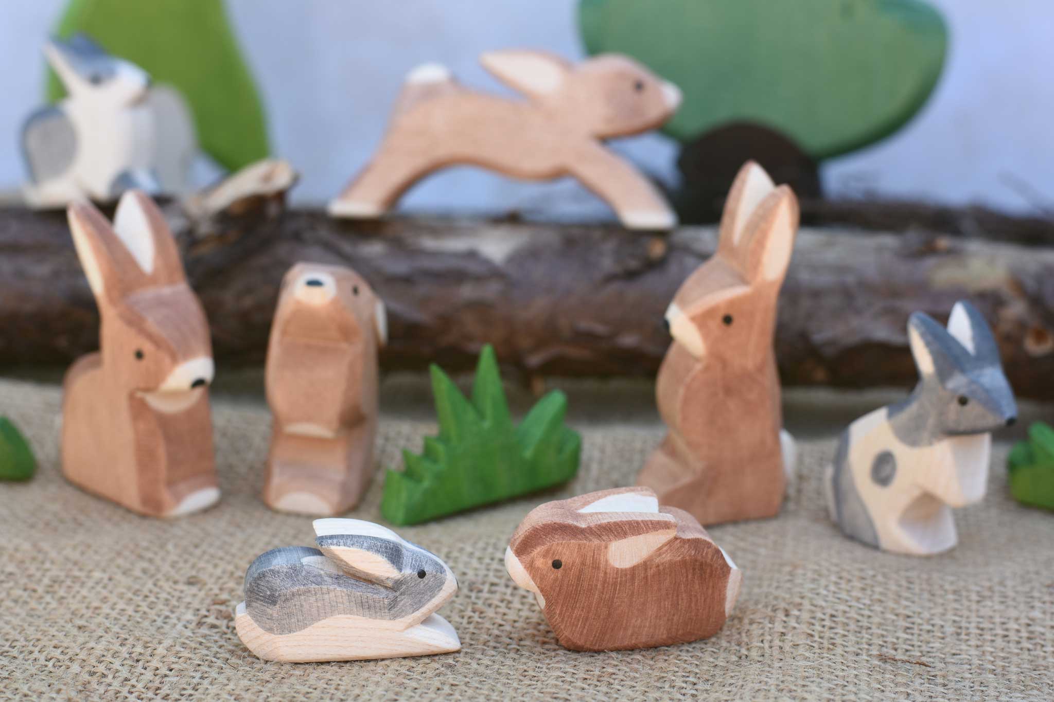 Two small Ostheimer rabbit wooden toy figures placed at the front of a small world play scene. One rabbit is  Black and White and the other is brown. Other rabbits from the collection can be seen in the background. Check out our full range of expertly crafted wooden toy figures and scenery here at Babipur.