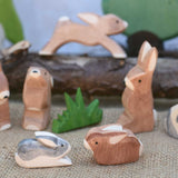 Two small Ostheimer rabbit wooden toy figures placed at the front of a small world play scene. One rabbit is  Black and White and the other is brown. Other rabbits from the collection can be seen in the background. Check out our full range of expertly crafted wooden toy figures and scenery here at Babipur.