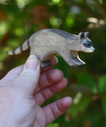 An Ostheimer running raccoon wooden toy figure held in an adult's hand to show scale. Check out our full range of expertly crafted wooden toy figures and scenery here at Babipur.