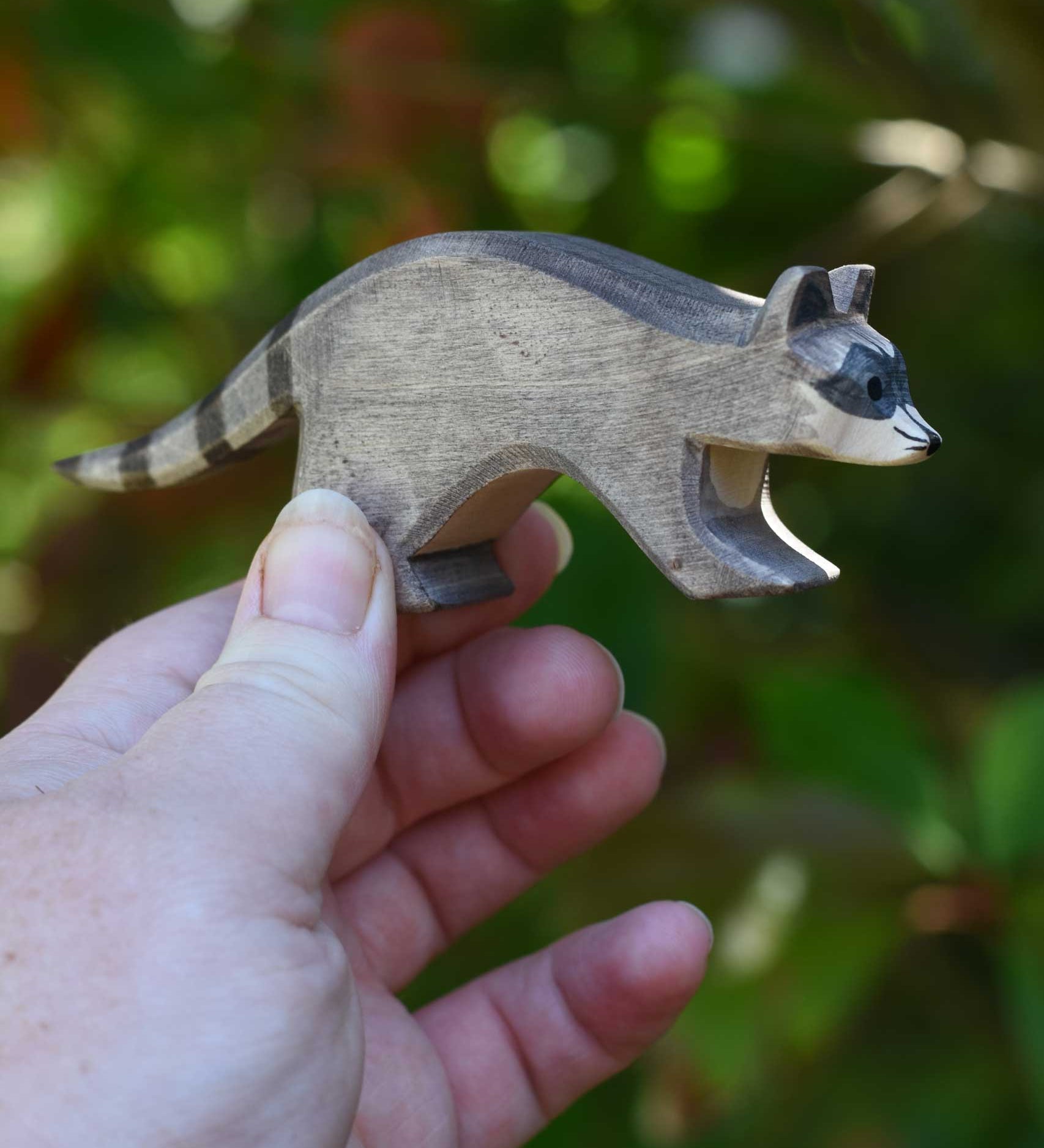 An Ostheimer running raccoon wooden toy figure held in an adult's hand to show scale. Check out our full range of expertly crafted wooden toy figures and scenery here at Babipur.