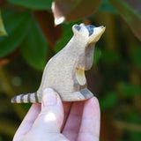 A sitting raccoon figure from Ostheimer being held up in an adult's hand to show scale. Check out our full range of expertly crafted wooden toy figures and scenery here at Babipur.