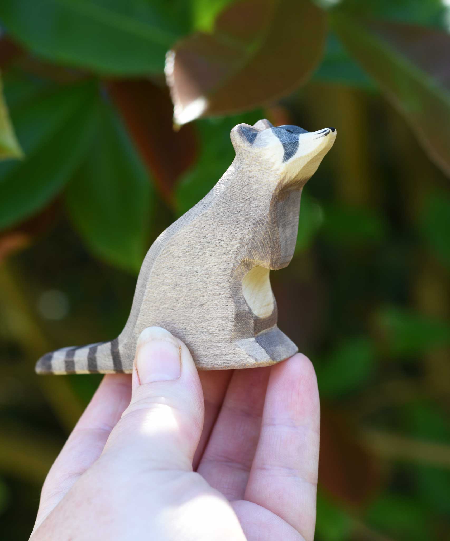 A sitting raccoon figure from Ostheimer being held up in an adult's hand to show scale. Check out our full range of expertly crafted wooden toy figures and scenery here at Babipur.