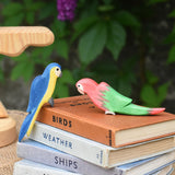 Two Ostheimer parrots, one blue, one red placed on a pile of old books.