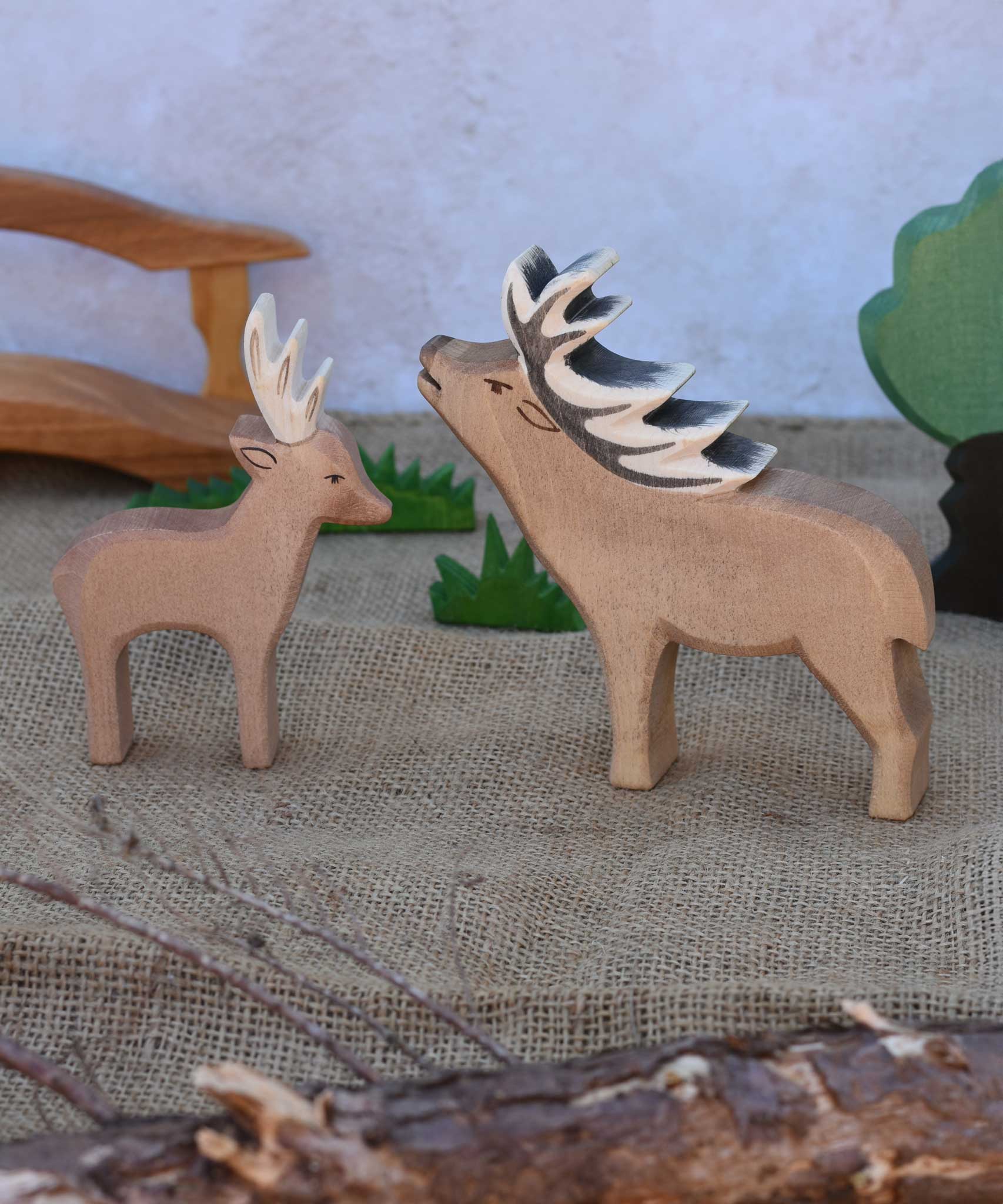 An Ostheimer male deer pictured nextto a red deer stag in a small world play scene with Ostheimer grass, oak tree and wooden toy bridge in the background. Check out our full range of expertly crafted wooden toy figures and scenery here at Babipur.