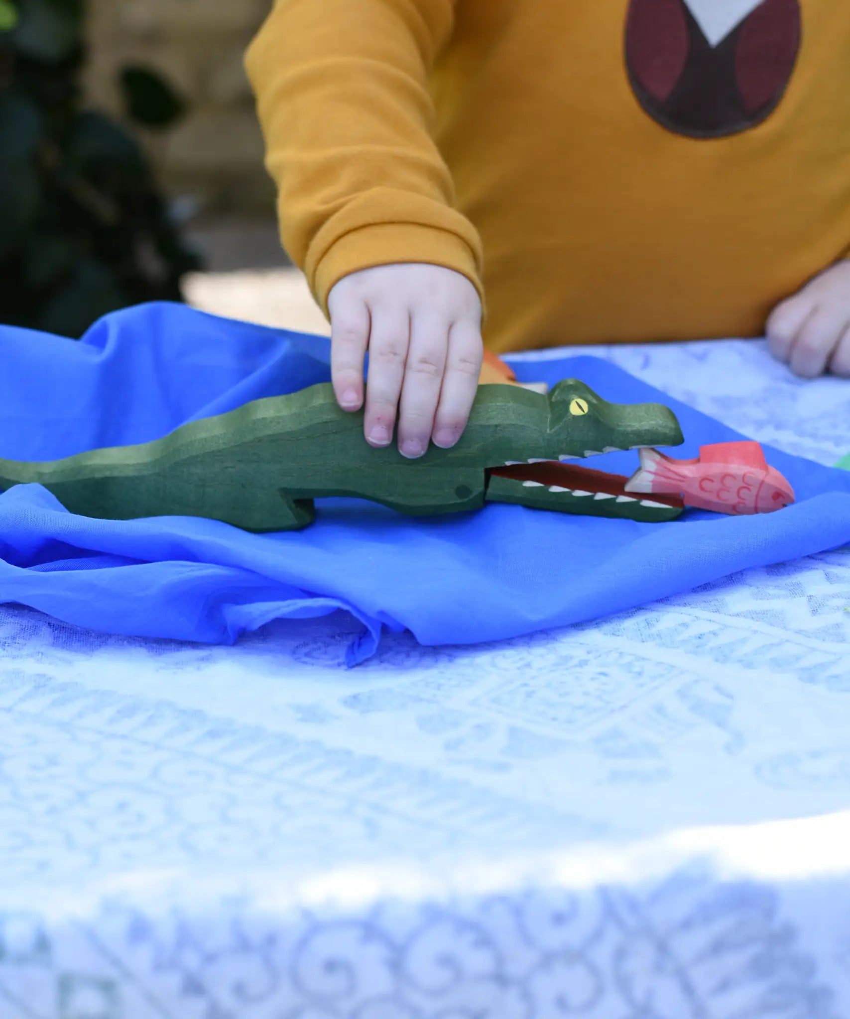Ostheimer crocodile wooden toy figure played with by a child. Red fish has been placed in the crocodiles mouth. 