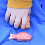 Ostheimer red fish figure placed on a blue Laura's cotton play cloth. A child's hand can be seen behind picking the yellow fish up.