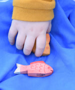 Ostheimer red fish figure placed on a blue Laura's cotton play cloth. A child's hand can be seen behind picking the yellow fish up.