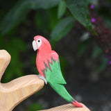 An Ostheimer red parrot wooden toy figure placed on a branch of the Ostheimer bird tree. 