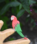 An Ostheimer red parrot wooden toy figure placed on a branch of the Ostheimer bird tree. 