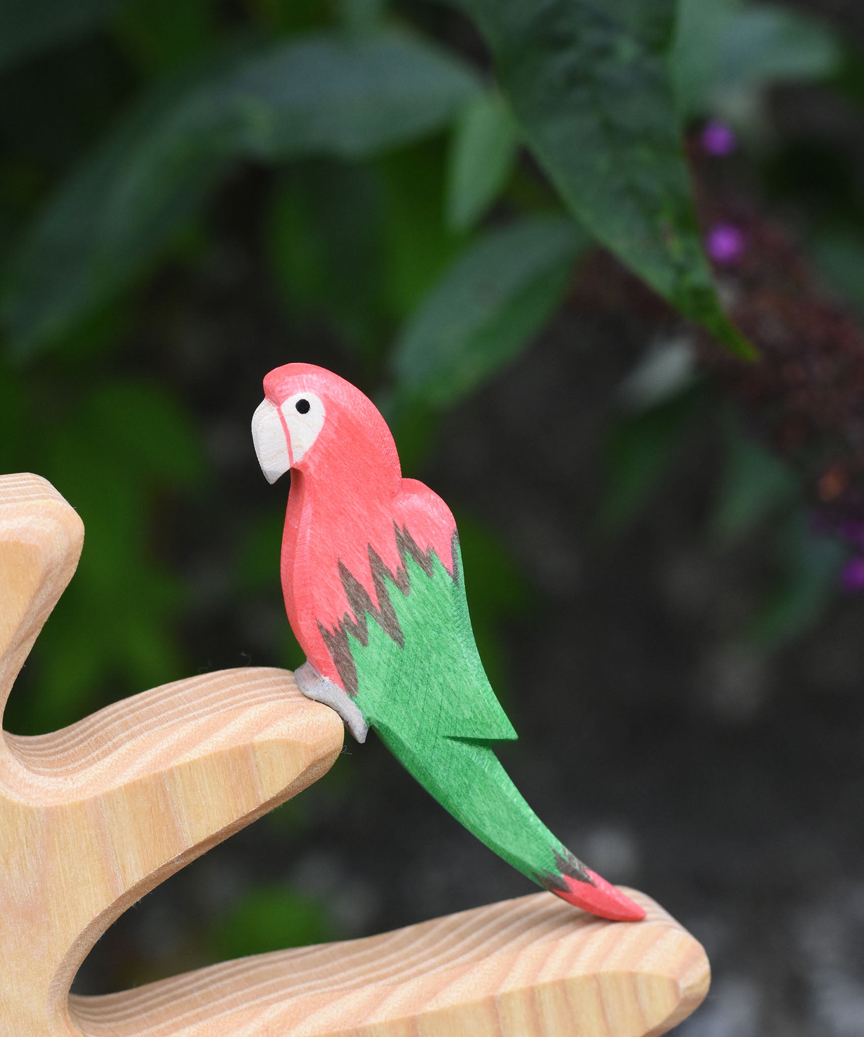 An Ostheimer red parrot wooden toy figure placed on a branch of the Ostheimer bird tree. 