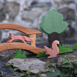 sitting and running red squirrel wooden toy figures placed in a small world play scene set up on a stone wall outdoors.  Check out our full range of expertly crafted wooden toy figures and scenery here at Babipur. 