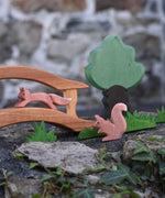 sitting and running red squirrel wooden toy figures placed in a small world play scene set up on a stone wall outdoors.  Check out our full range of expertly crafted wooden toy figures and scenery here at Babipur. 