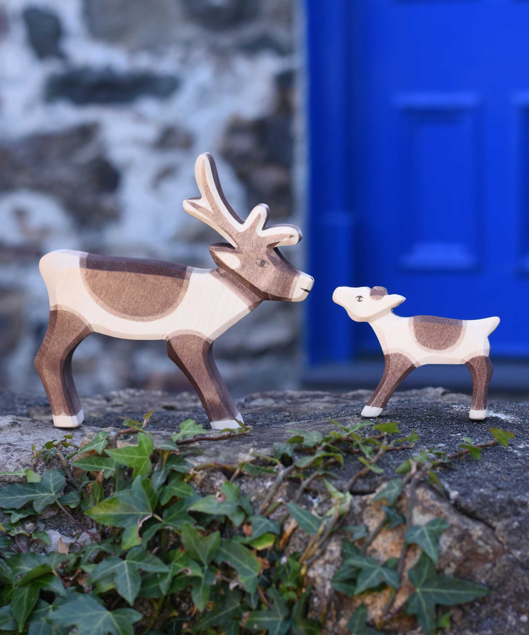 An Ostheimer reindeer and reindeer calf placed on a stone wall outdoors. Check out our full range of expertly crafted wooden toy figures and scenery here at Babipur.