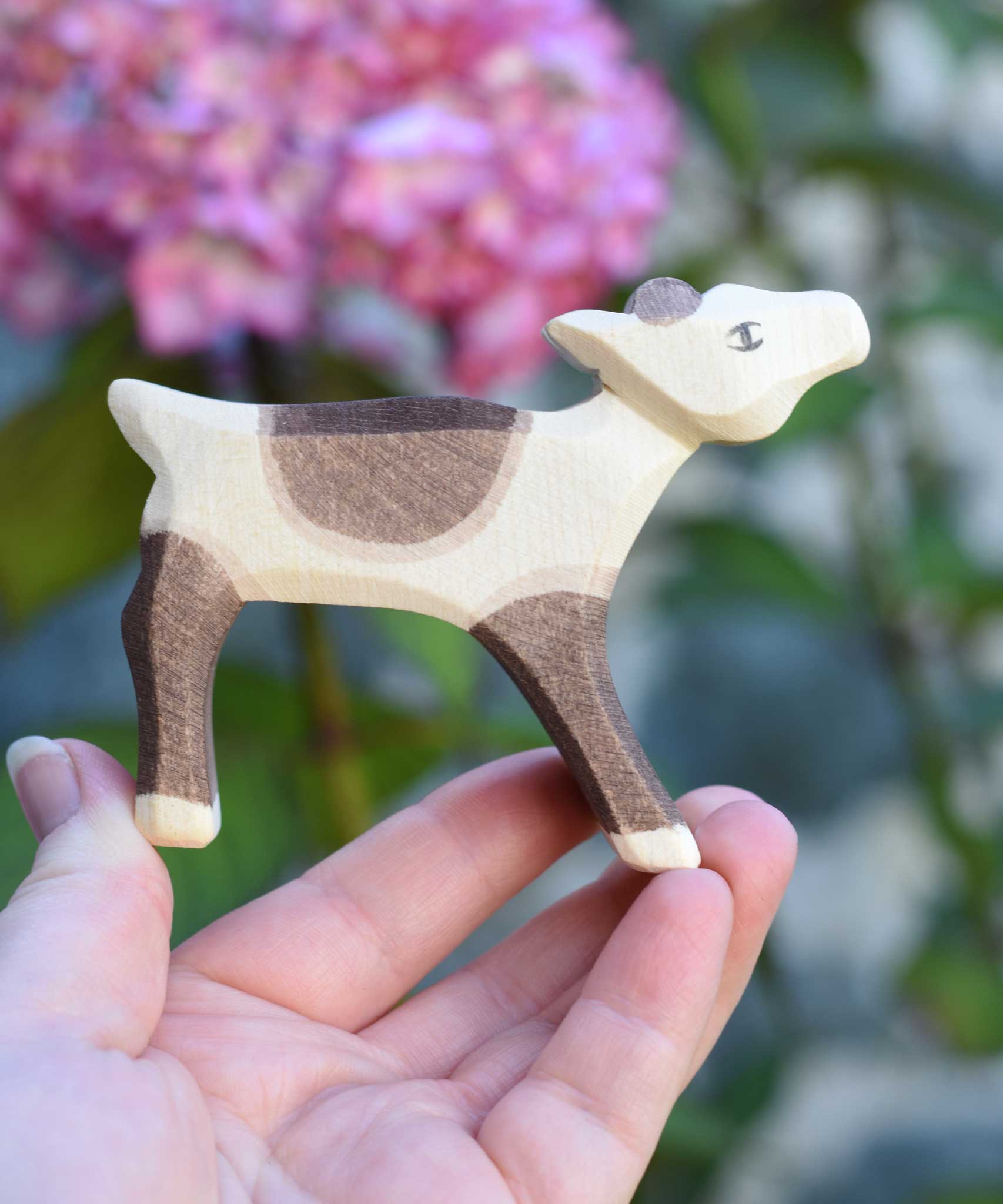 An Ostheimer reindeer calf wooden toy figure shown in an adult's hand for scale. Check out our full range of expertly crafted wooden toy figures and scenery here at Babipur.