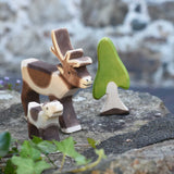 An Ostheimer reindeer and reindeer calf placed on a stone wall outdoors next to an Ostheimer birch tree. Check out our full range of expertly crafted wooden toy figures and scenery here at Babipur.