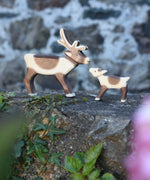 An Ostheimer reindeer and reindeer calf placed next to each other on a stone wall outdoors. Check out our full range of expertly crafted wooden toy figures and scenery here at Babipur.