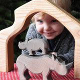 The small Ostheimer rhino wooden toy figure stacked on top of the large rhino. A child can be seen looking on in the background. These wooden figures are part of a wide range of expertly hand crafted wooden toys here at Babipur.