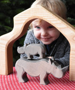 The small Ostheimer rhino wooden toy figure stacked on top of the large rhino. A child can be seen looking on in the background. These wooden figures are part of a wide range of expertly hand crafted wooden toys here at Babipur.