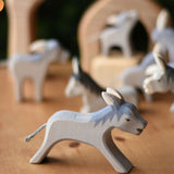 Ostheimer running donkey wooden toy figure placed on a wooden surface with other donkeys in the background.  Ostheimer's range of hand crafted, heirloom quality wooden toys are available to buy at Babipur. 