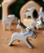 Ostheimer running donkey wooden toy figure placed on a wooden surface with other donkeys in the background.  Ostheimer's range of hand crafted, heirloom quality wooden toys are available to buy at Babipur. 