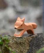 Ostheimer running fox wooden toy figure placed on a stone wall outdoors. 