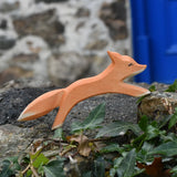Ostheimer running fox wooden toy figure placed on a stone wall outdoors. 