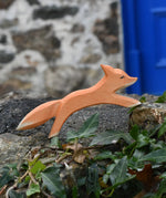 Ostheimer running fox wooden toy figure placed on a stone wall outdoors. 