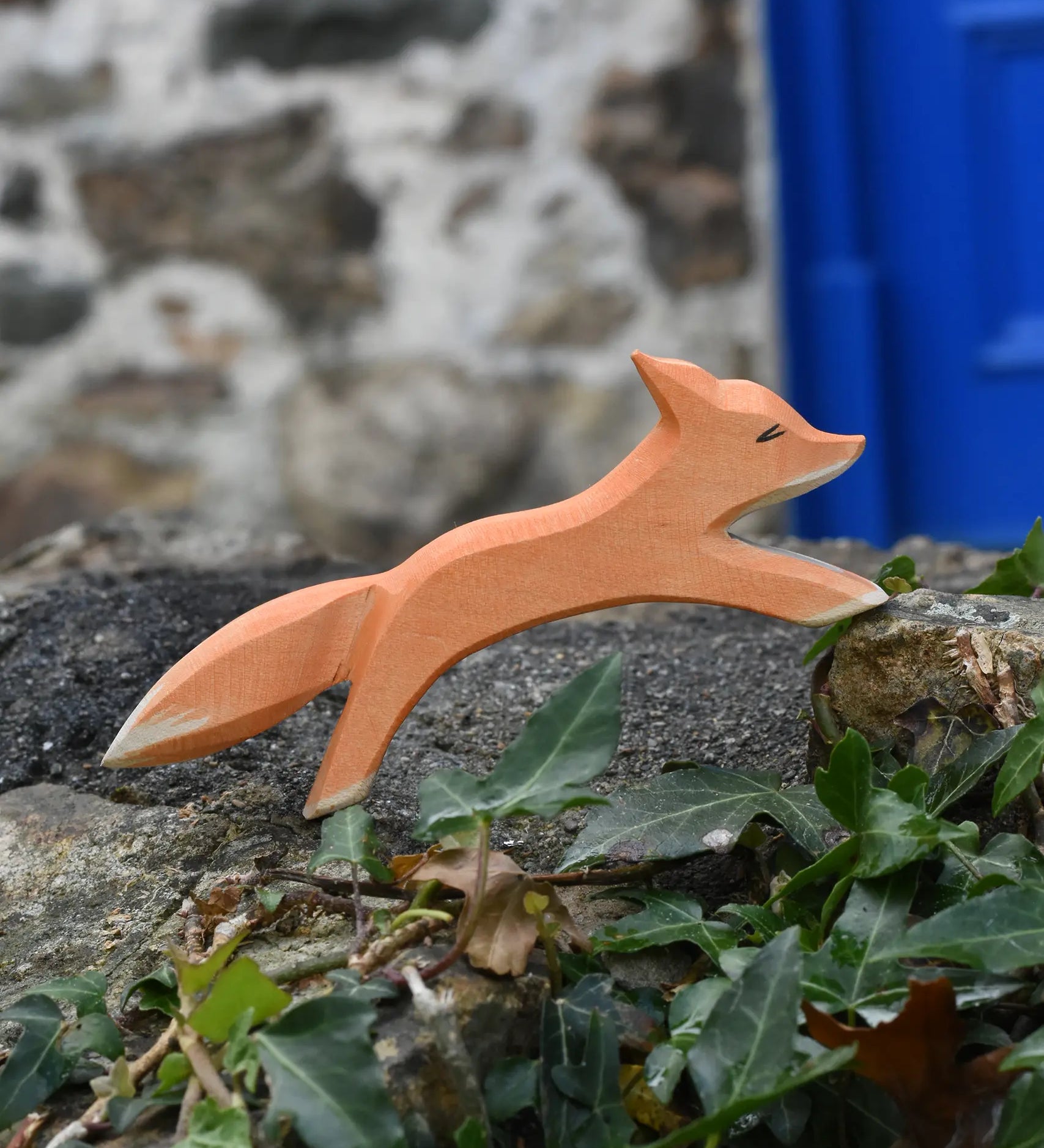 Ostheimer running fox wooden toy figure placed on a stone wall outdoors. 